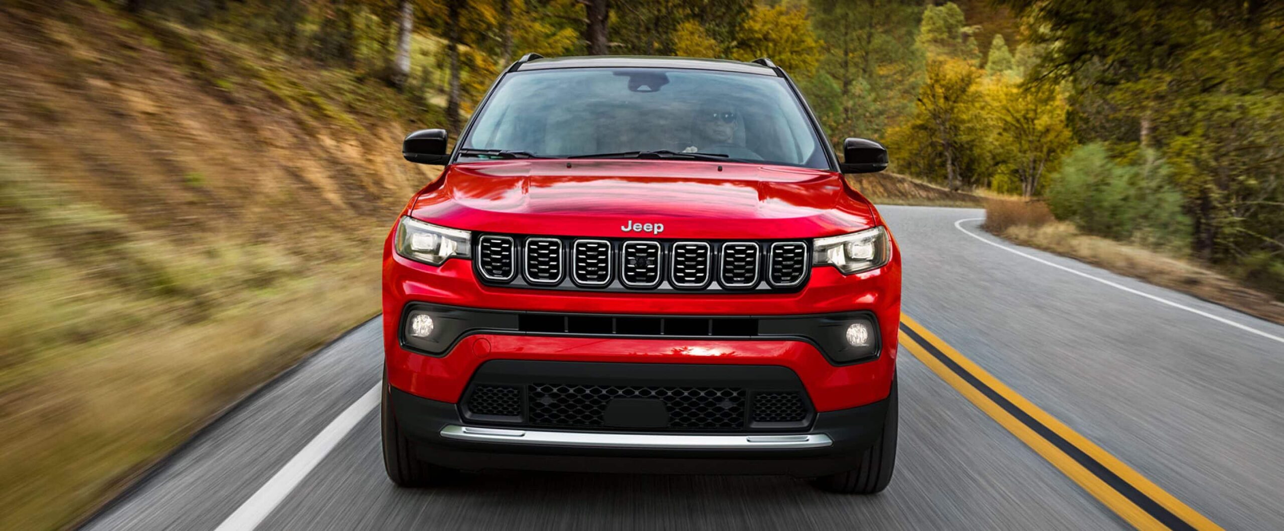 Front view of a red 2025 Jeep Compass driving down the road