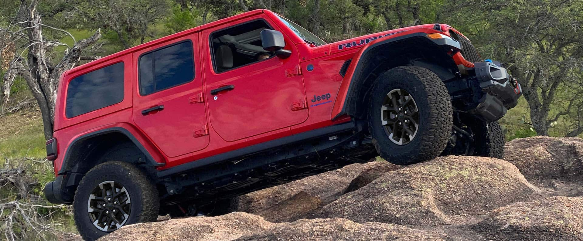 A red 2025 Jeep Wrangler driving over a rocky road.