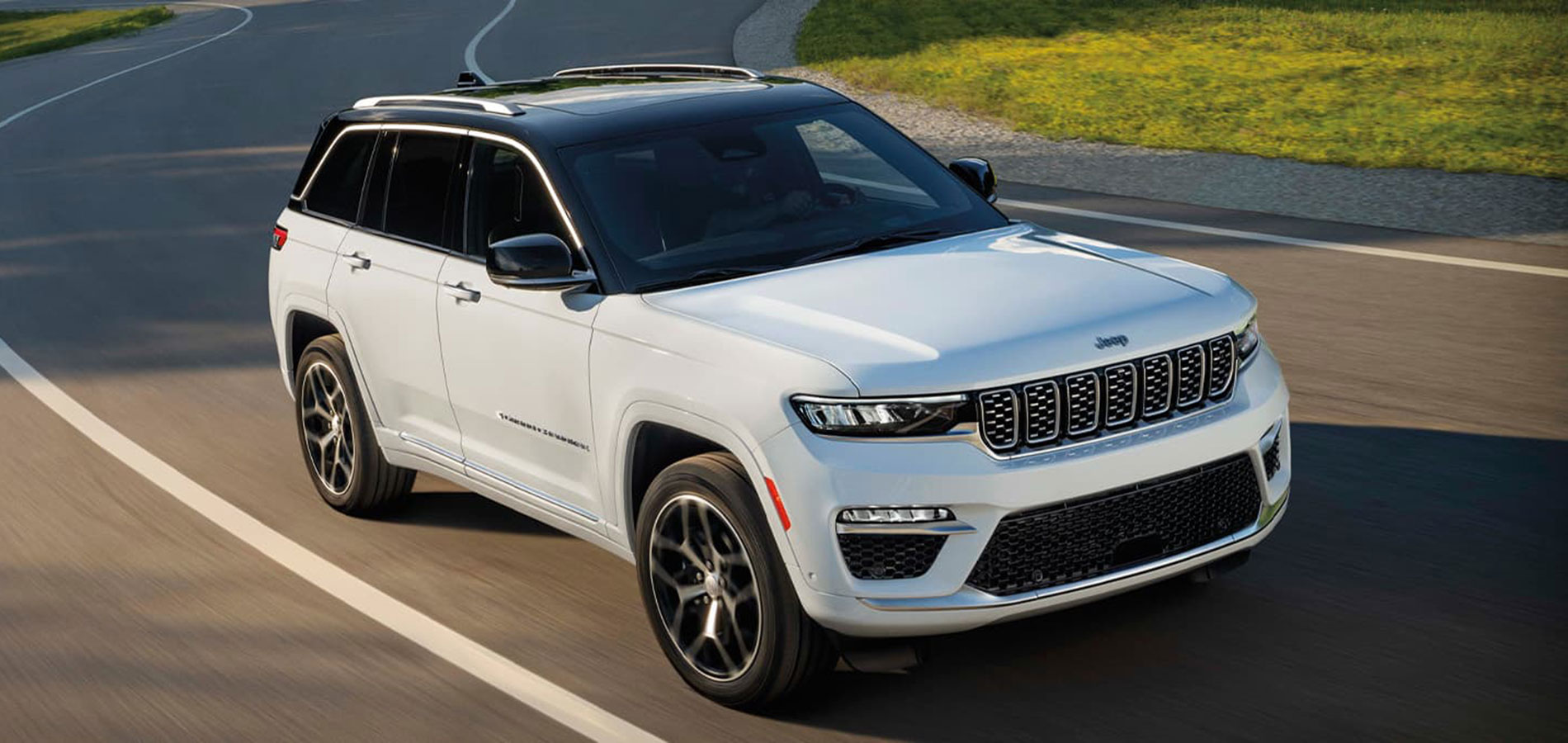 A white 2025 Jeep Grand Cherokee driving down a bend in the road.